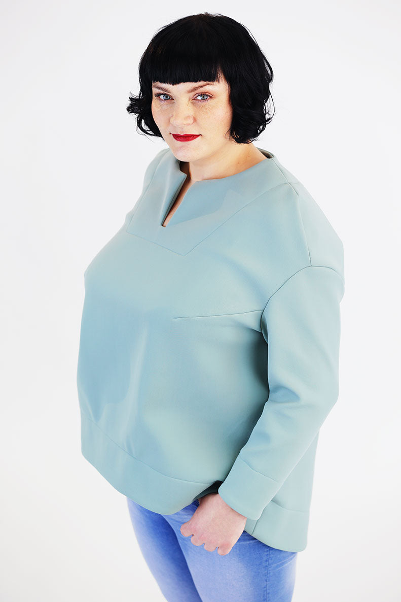 Vor einem weißen Hintergrund steht eine frau in ihrem selbst genähtem türkisfarbenem Shirt