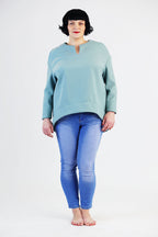 eine Frau mit kurzen schwarzen Haaren steht in ihrem selbst genähtem Shirt auf einem weißen Hintergrund