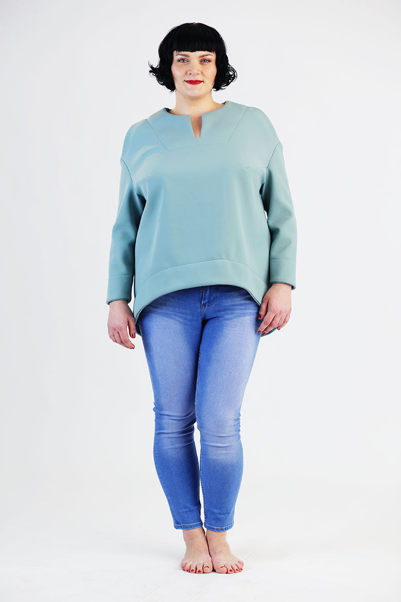 eine Frau mit kurzen schwarzen Haaren steht in ihrem selbst genähtem Shirt auf einem weißen Hintergrund