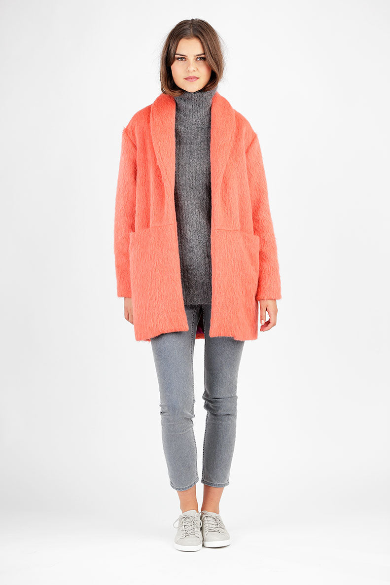 Eine Frau die einen rosa Mantel sowie eine graue Jeans trägt