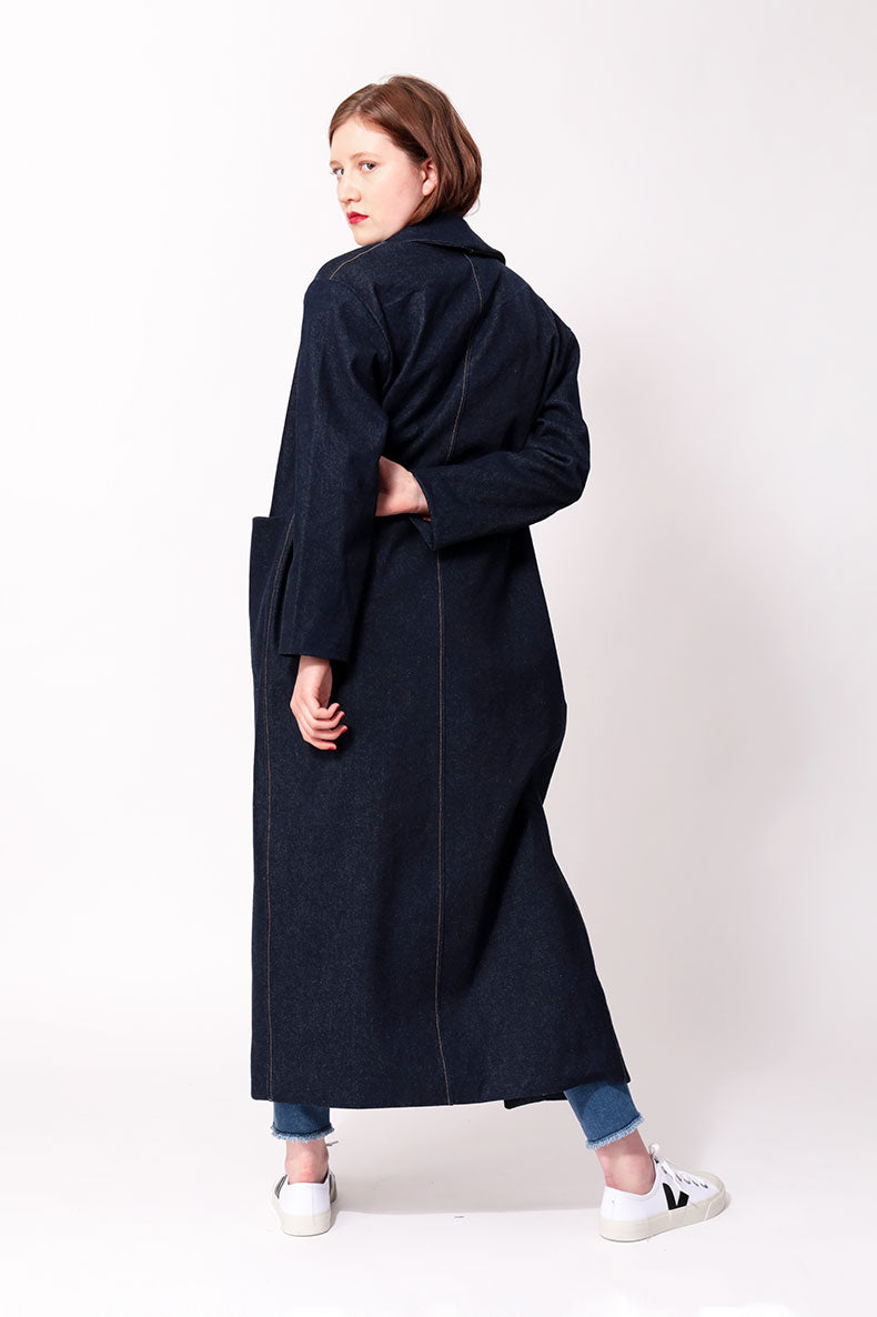 Eine Frau die einen blauen Mantel trägt schaut über ihre Schulter in die Kamera