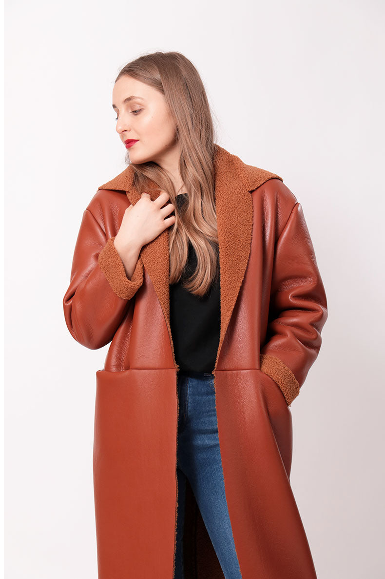 eine Frau, die einen braunen Kunstedermantel und Jeans trägt.
