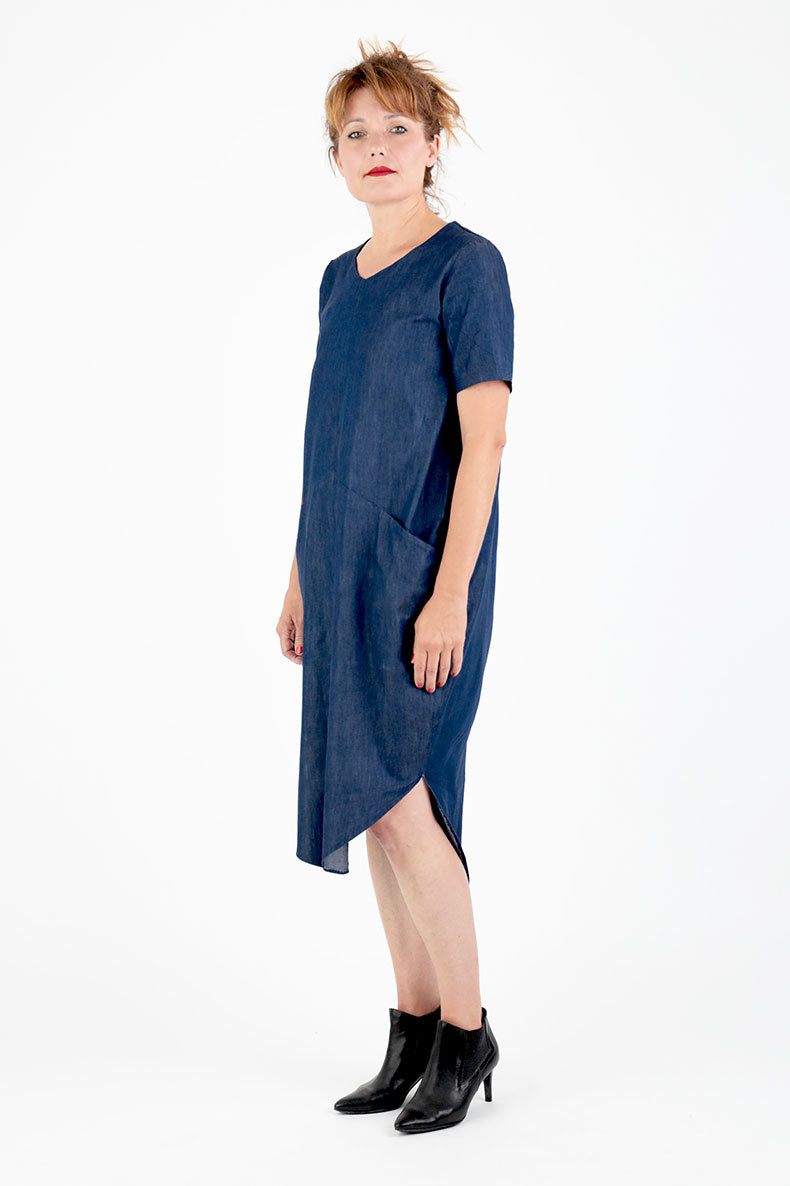 Vor einem weißen Hintergrund steht eine Frau in einem blauen Kleid