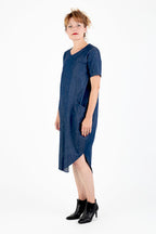 Vor einem weißen Hintergrund steht eine Frau in einem blauen Kleid