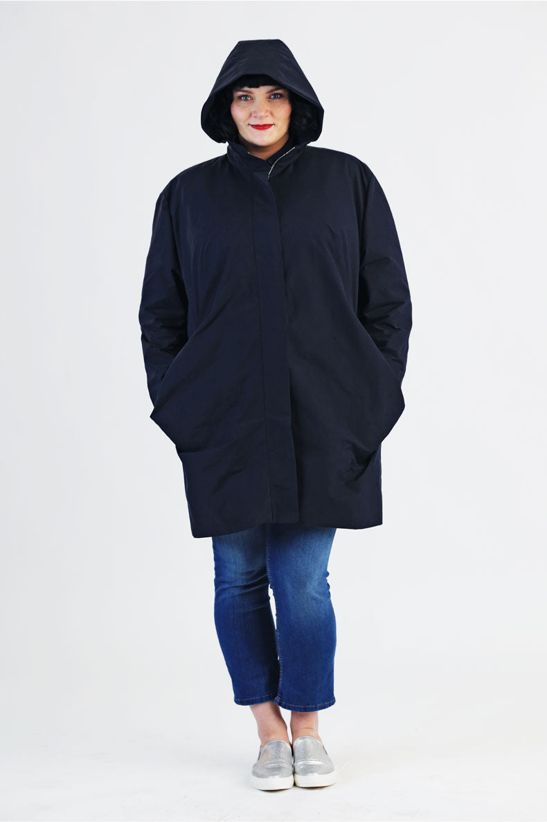vor einer weißen Wand steht eine Frau welche einen Blauen plussize Parka trägt