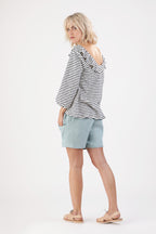 eine junge Frau welche ein gestreiftes Shirt trägt blickt über ihre Schulter in die Kamera