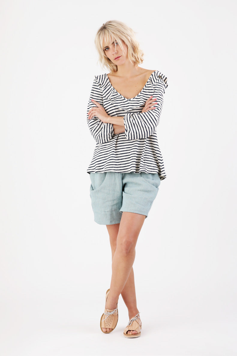 Mit verschränkten Armen schaut eine Frau welche ein Gestreiftes Shirt trägt in die Kamera