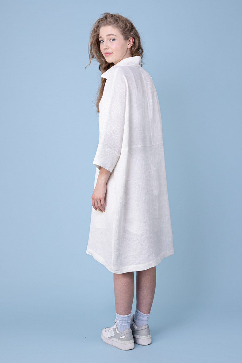 lächelnd kuckt ein vor einem blauen Hintergrund stehendes Mädchen über ihre Schulter in die Kamera