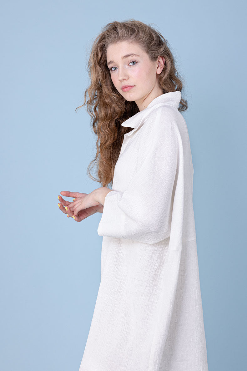 vor einem blauem Hintergrund steht ein Mädchen welches ein weißes Kleid trägt