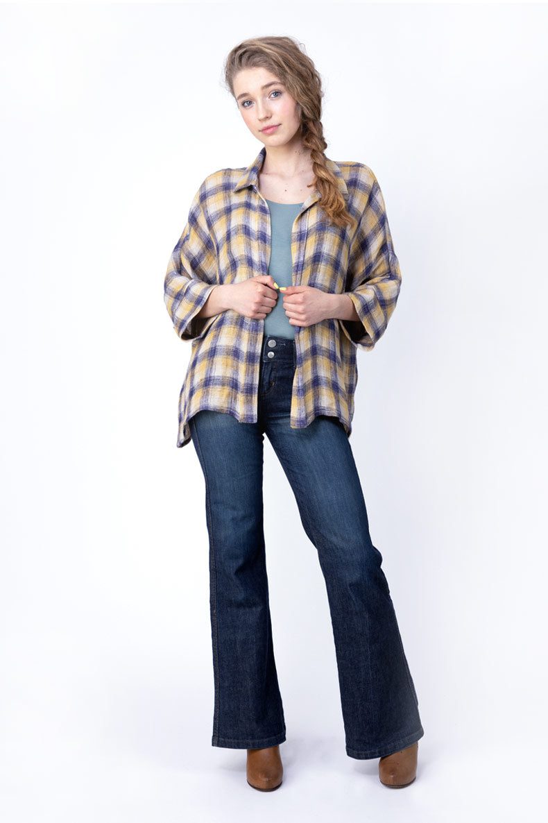 eine Dame posiert vor einer weißen Wand mit blauer Jeans und gelb karierter Bluse