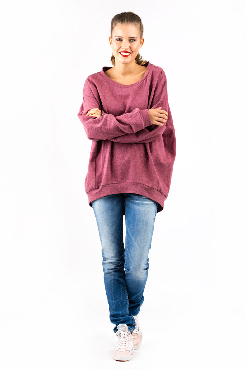 vor einer weißen Wand steht eine lächelnde Dame gekleidet in ein oversized Shirt und eine blaue Jeans