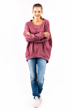 vor einer weißen Wand steht eine lächelnde Dame gekleidet in ein oversized Shirt und eine blaue Jeans