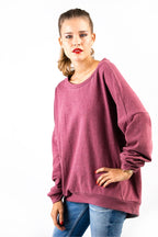 eine Frau in einem magentafarbenem Shirt stützt ihre Hand auf der Hüfte ab und schaut in die Kamera