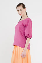 eine Frau mit zaghaften lächeln trägt ihr aus einem Schnittmuster selbst genähtes pinkes Shirt
