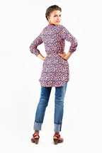 vor einer weißen Wand steht eine Frau mit Rücken in Richtung Kamera und lächelt über ihre Schulter