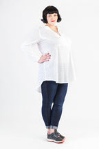 vor einem weißen Hintergrund steht eine Frau mit weißer Tunika und blauer Jeans